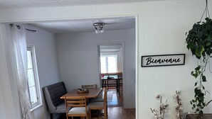 A spacious room with wooden flooring, a dining table with chairs, a sofa, and a 'Bienvenue' sign on the wall.