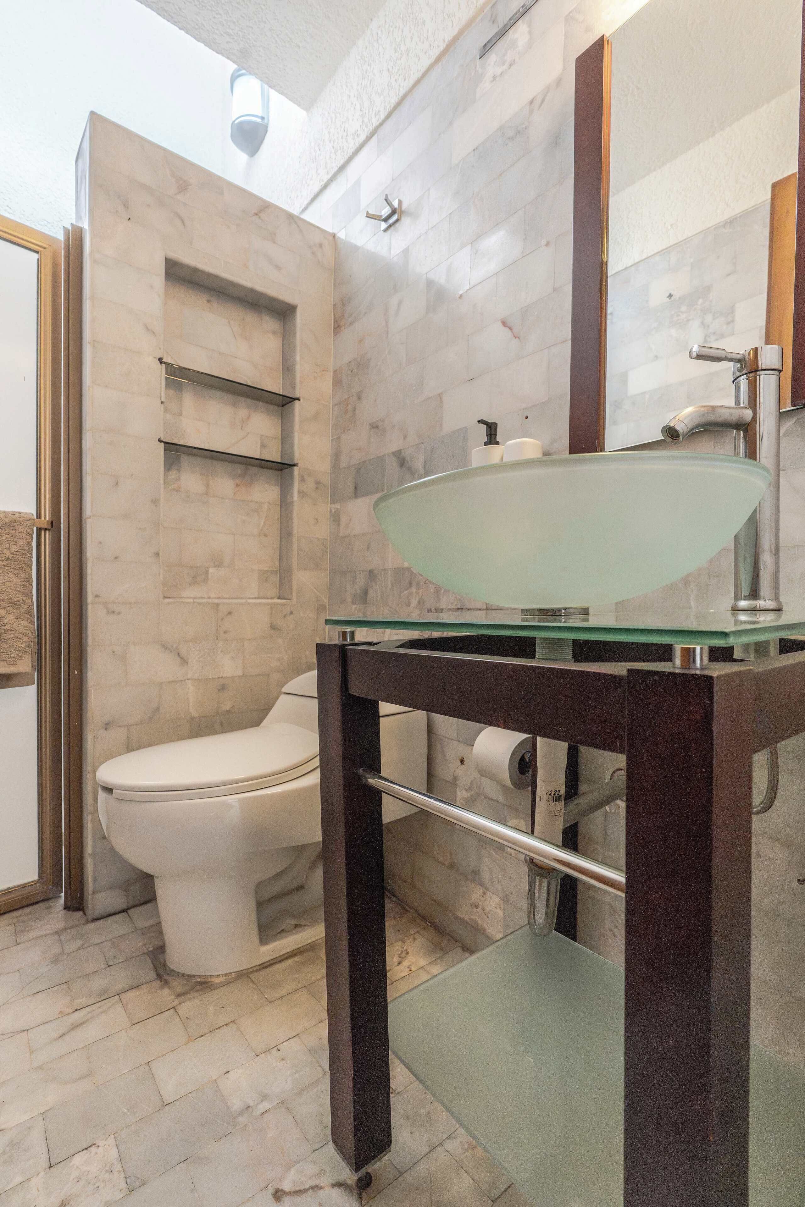 A bathroom with a glass sink, a toilet, and a shower area.