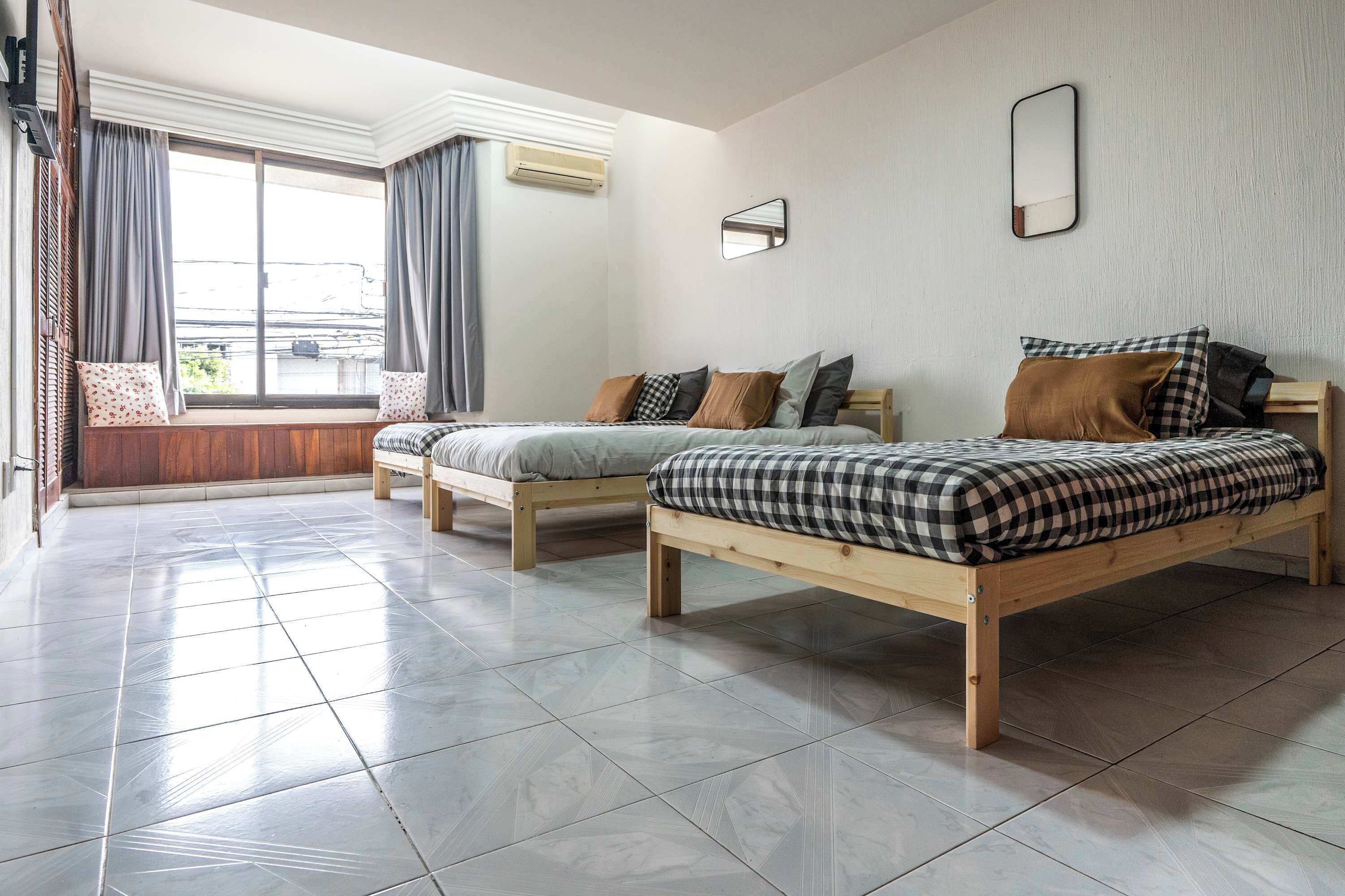 A hotel room with two wooden beds, a large window with curtains, and a tiled floor.