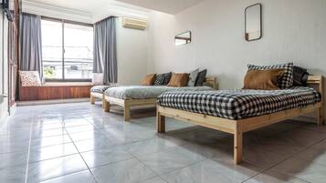 A hotel room with two wooden beds, a large window with curtains, and a tiled floor.