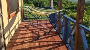 Une terrasse en bois, agrémentée d’un hamac et d’une rambarde en métal, qui offre une vue sur un paysage verdoyant et luxuriant.