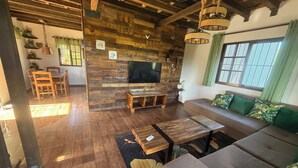 Un salon chaleureux avec un plancher en bois, un canapé, un téléviseur fixé à un mur en bois, et un coin repas avec des chaises et une table.