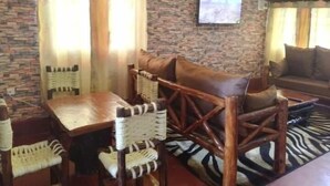 Un salon chaleureux avec un mur en pierre, une table en bois entourée de chaises, un tapis à motifs zébrés et un canapé agrémenté de coussins.