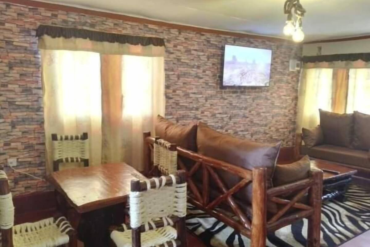 Ein gemütlicher Wohnbereich mit einer Steinwand, einem Holztisch mit Stühlen, einem zebra-gemusterten Teppich und einer Couch mit Kissen.