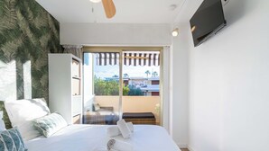 Habitación de hotel con cama, ventilador de techo, televisión montada en la pared y vista al balcón exterior.