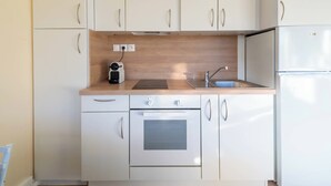 Una cocina compacta con armarios blancos, horno empotrado, lavabo y cafetera.