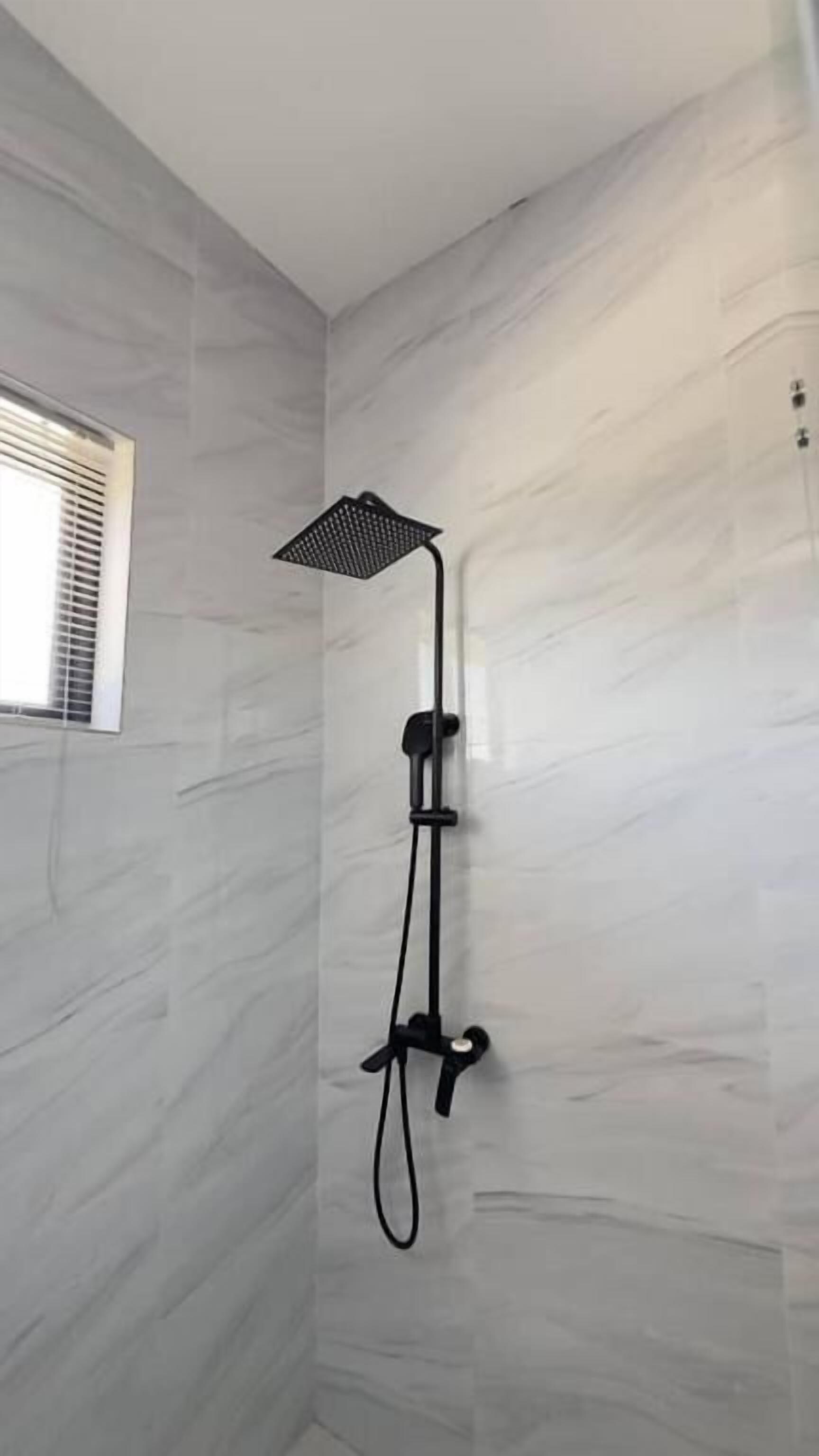 A shower with a black handheld showerhead mounted on a wall with a marble-like texture.