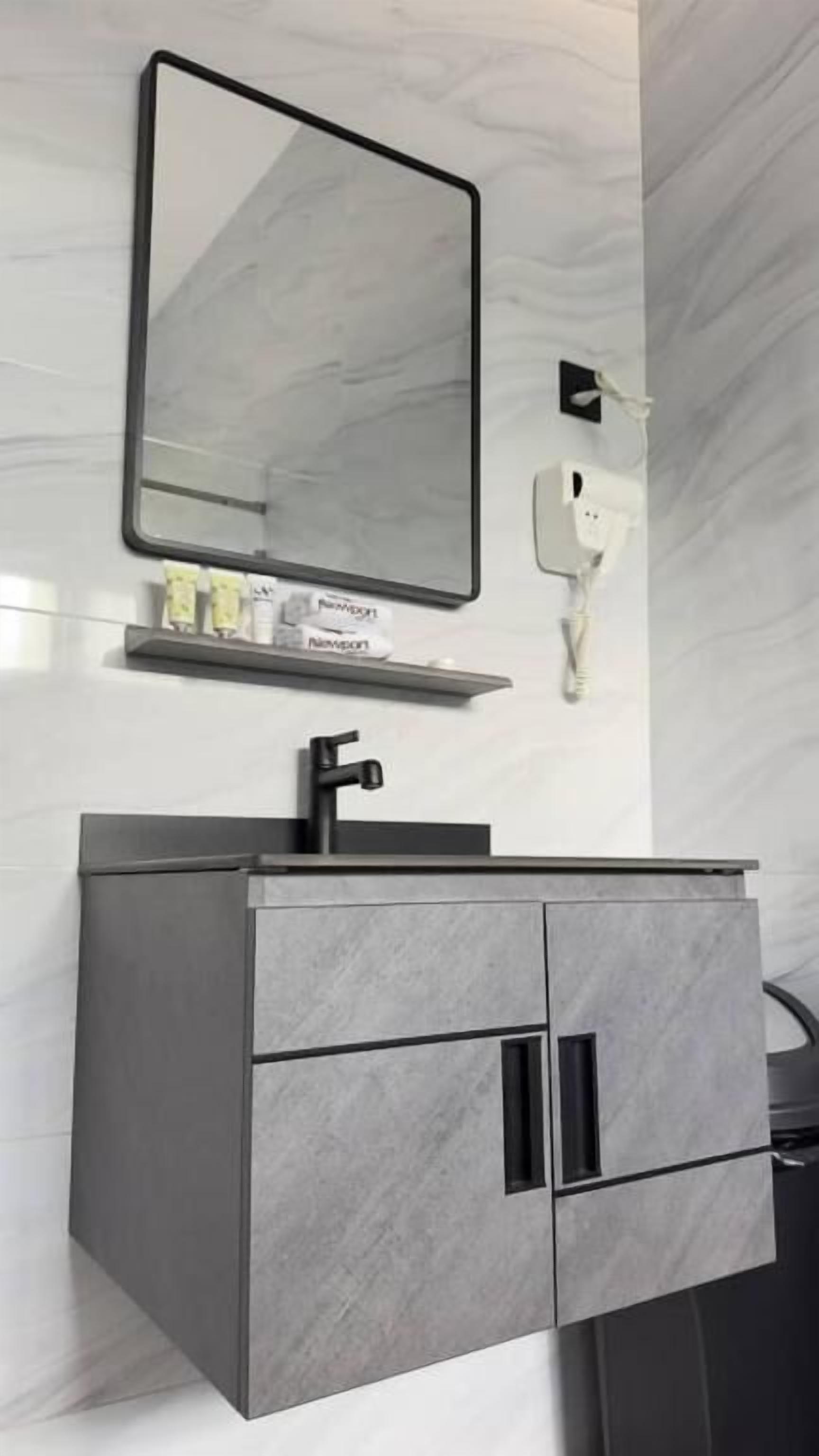 Un baño moderno con un tocador gris, un espejo y una lámpara de pared.