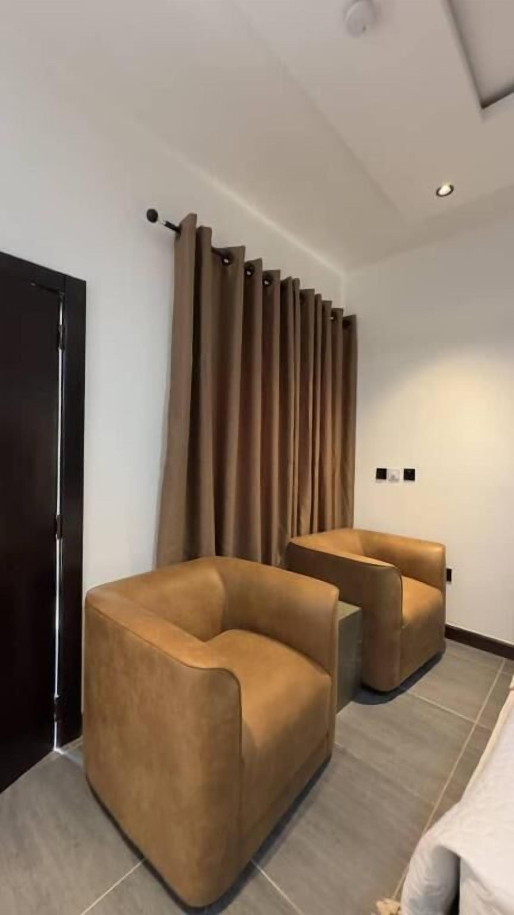 A modern hotel room with a large window, a dark door, and a brown sofa.