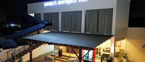 A building with a sign reading 'Serwaa's Conference Hall' and a covered outdoor area with chairs and tables.