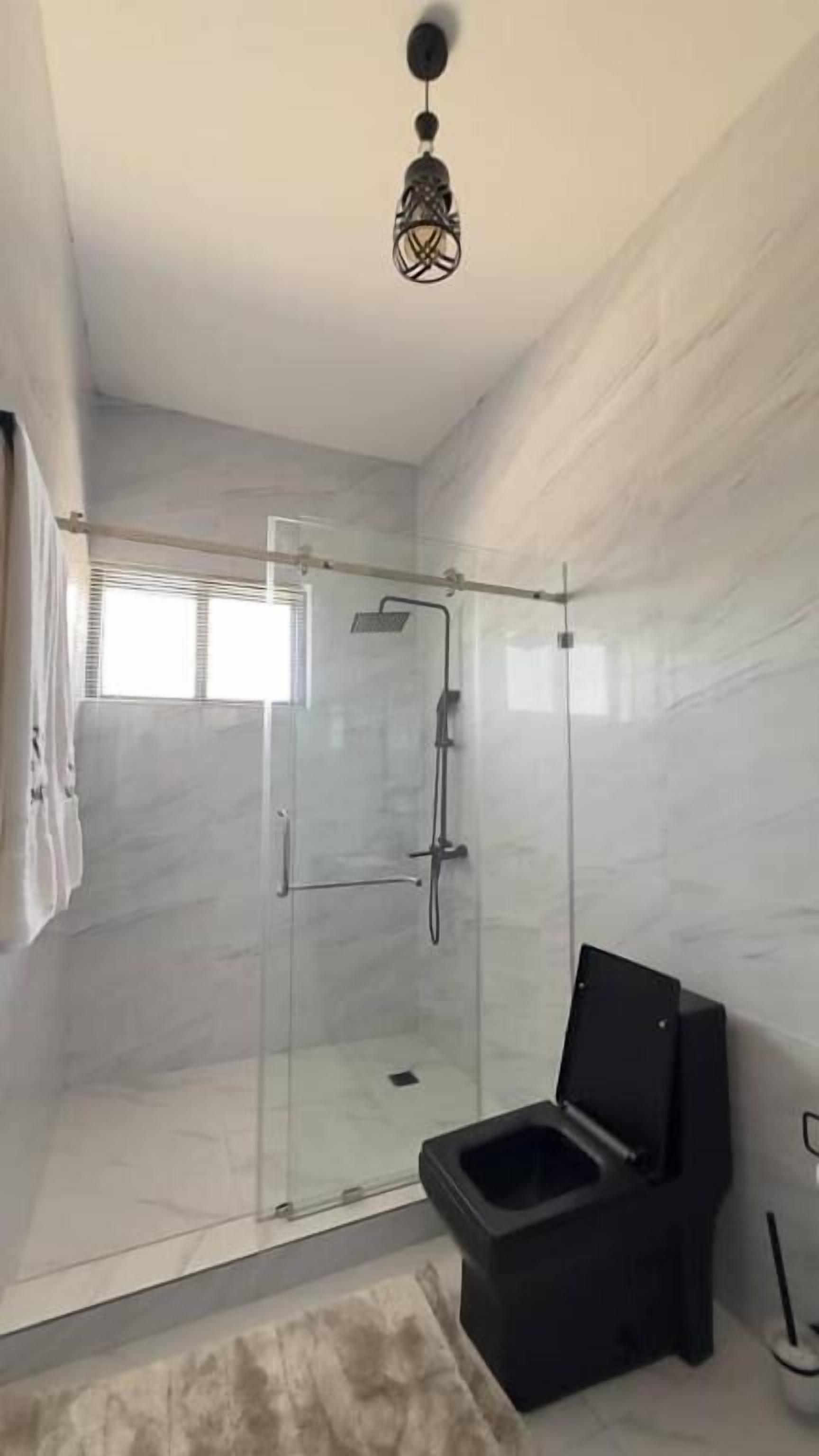 A modern bathroom with a glass-enclosed shower, a black toilet, and a unique ceiling light fixture.