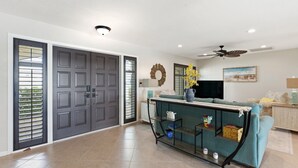 Un amplio salón con sofá, mesa de centro y televisor. Se observan dos puertas y un ventilador de techo.