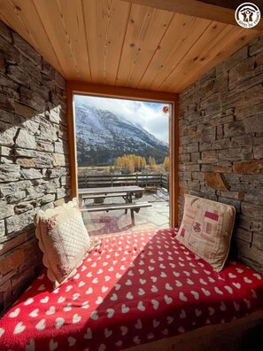 Una habitación acogedora con pared de piedra, techo de madera y una cama con manta de estampado de corazones rojos.