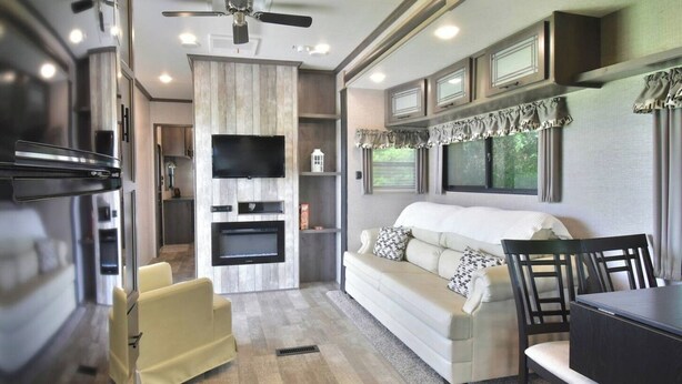 A modern RV interior with a living area, kitchenette, and a ceiling fan.