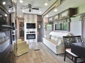 A modern RV interior with a living area, kitchenette, and a ceiling fan.