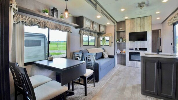A modern RV interior with a dining area, seating, kitchen, and large windows. - Mins from the Lake! Camper King Bed • Firepit (Decatur)