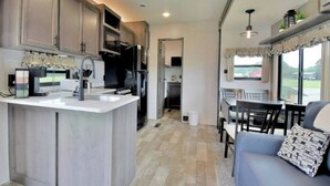 A compact kitchen with a central island, a dining area with a table and chairs, and a sofa with a patterned cushion. - Mins from the Lake! Camper King Bed • Firepit (Decatur)