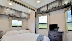 A bedroom with a large bed, a dresser, a television, and windows with curtains. - Mins from the Lake! Camper King Bed • Firepit (Decatur)