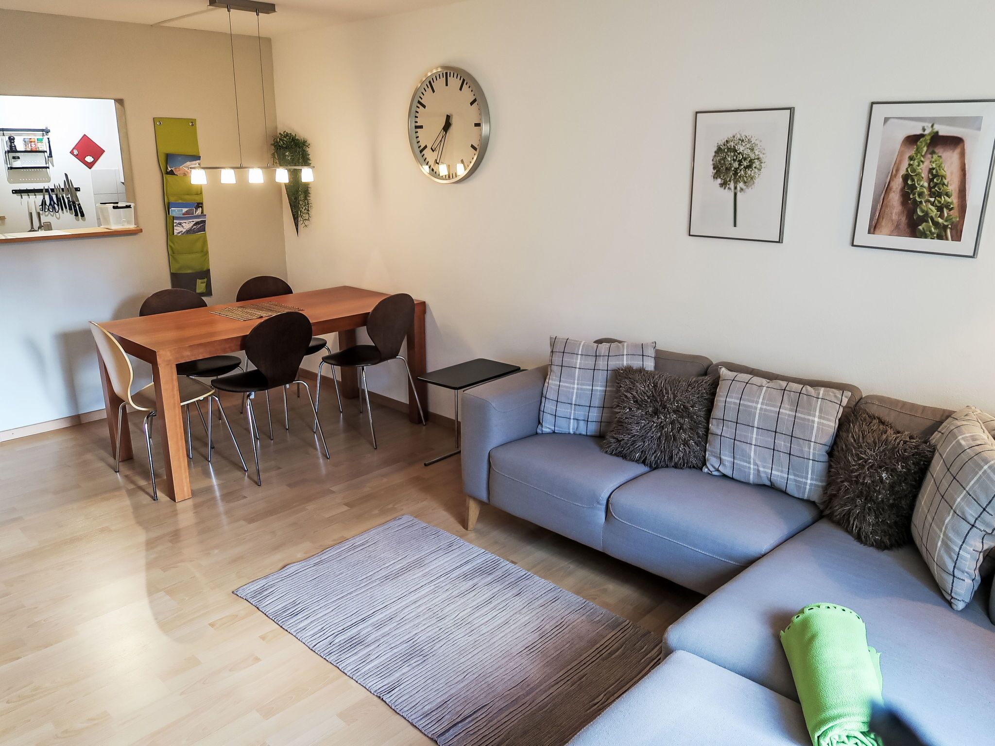 A modern living room with a wooden dining table, grey sofa, and a grey rug.