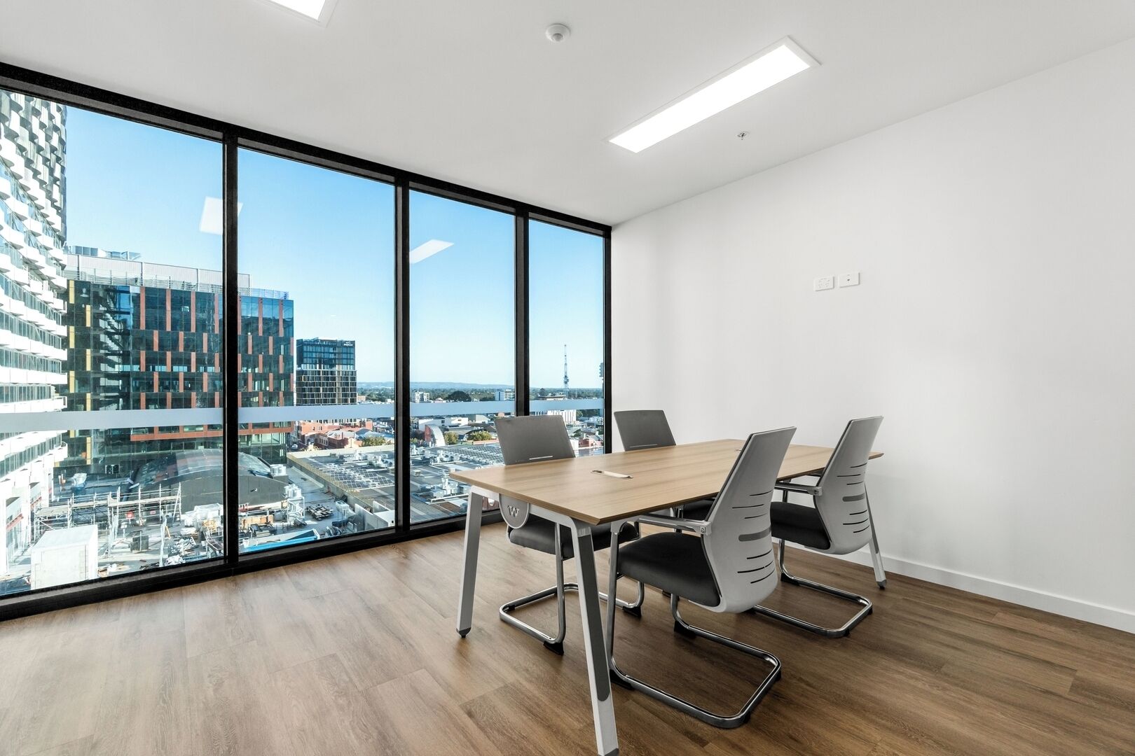 A modern conference room with a large window, a wooden table, and four chairs.