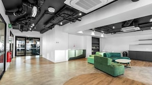 A modern office space with a wooden floor, green sofas, a round table, and a kitchenette area. - Luxe 1+1 Apt | Huge Balcony+BBQ  | Adelaide CBD (Adelaide)