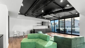 A modern office space with green sofas, a kitchen area, and large windows offering a city view. - Luxe 1+1 Apt | Huge Balcony+BBQ  | Adelaide CBD (Adelaide)