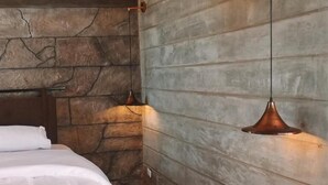 Une chambre avec un mur en pierre, un lit recouvert de draps blancs et deux lampes suspendues.