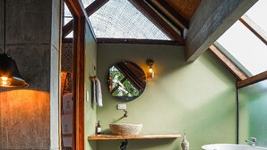 Ein Badezimmer mit Steinwaschbecken, einer Badewanne, einem Spiegel und einem Oberlicht.