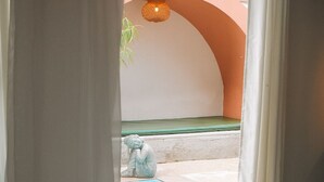Blick auf einen Swimmingpool mit einer Statue, einer Hängeleuchte und einem teilweisen Blick in einen Raum mit einem gemusterten Boden.