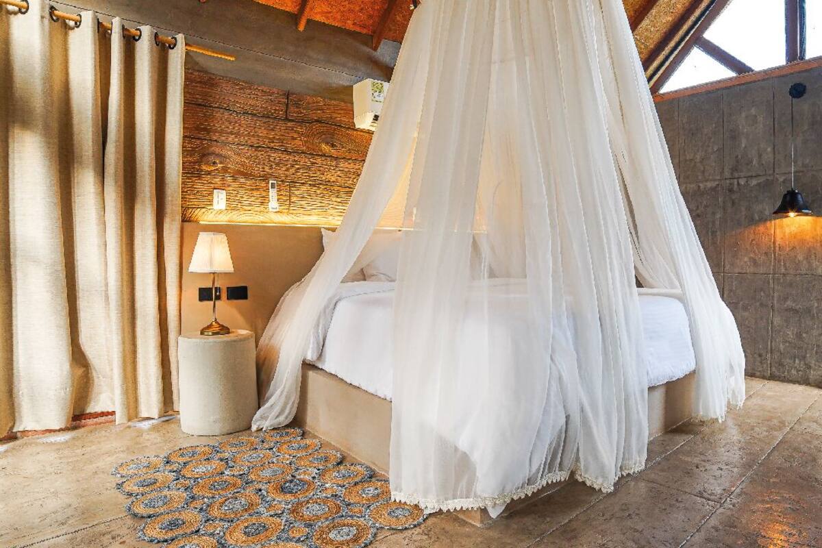 Un lit à baldaquin, une table de chevet avec une lampe, un tapis à motifs et un mur en pierre.