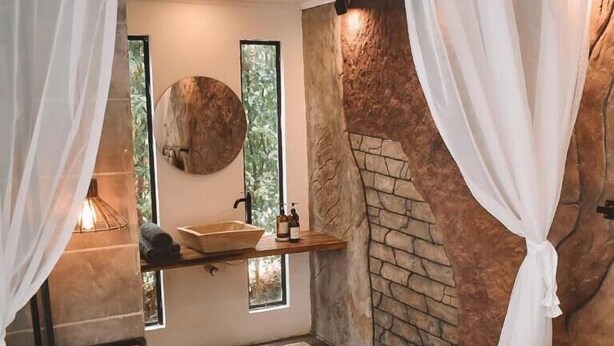 Ein Schlafzimmer mit Kamin aus Stein, einem Holzregal mit Pflegeprodukten und einem großen Fenster.