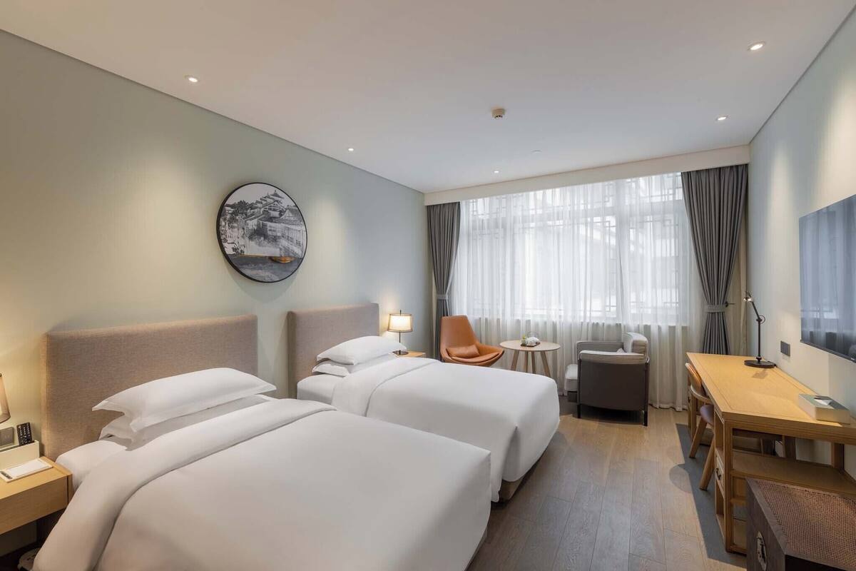 Habitación de hotel con dos camas, un escritorio, una silla, una mesita y un televisor.