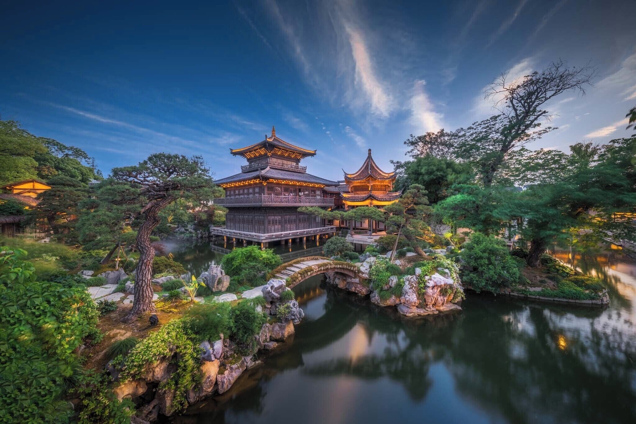 A traditional Chinese building with a large courtyard, a bridge, and a pond.