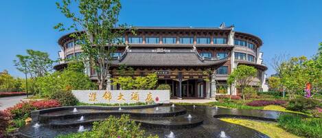 A traditional building with a curved roof and multiple windows, surrounded by a landscaped garden with a central water feature.