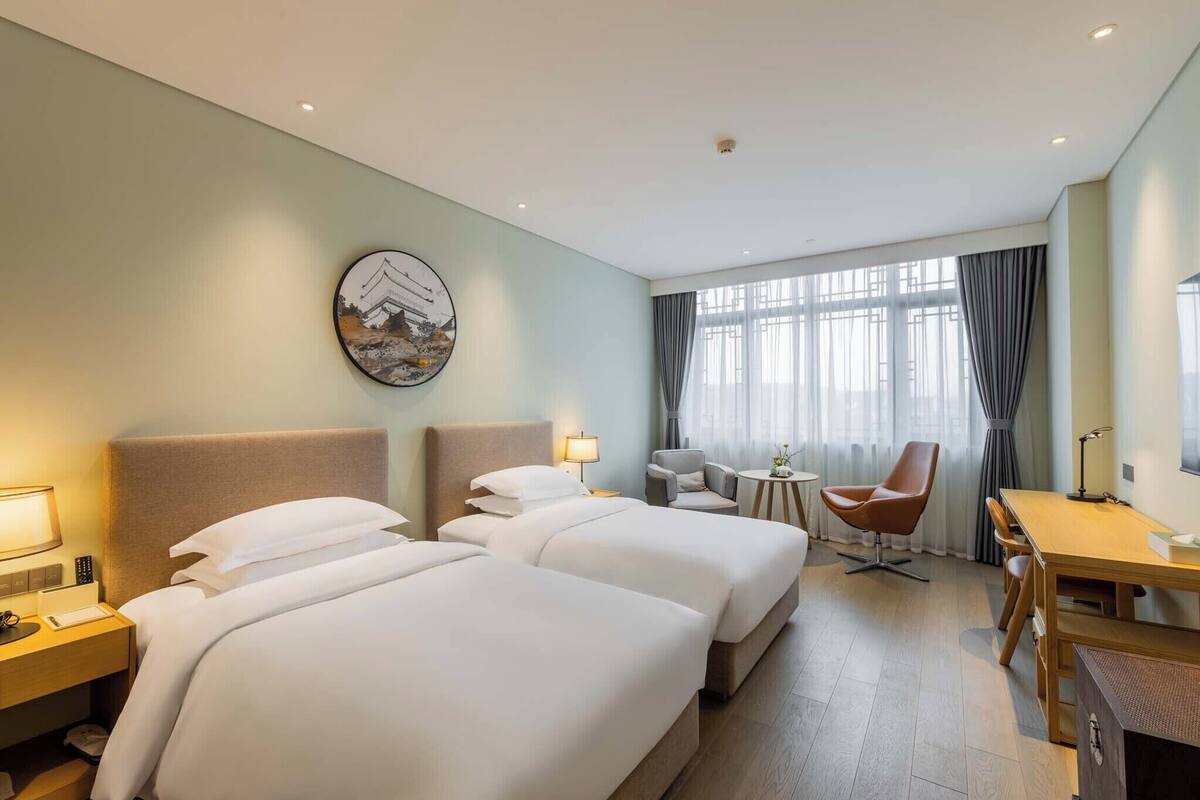 Habitación de hotel con dos camas, un escritorio, una silla y una mesita.