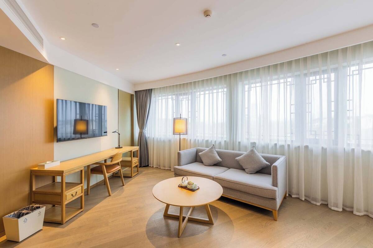 Una habitación de hotel moderna con sofá, escritorio, mesa de centro y televisor.