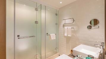 Un baño moderno con ducha de vidrio, lavamanos blanco y espejo, y un perchero para toallas.