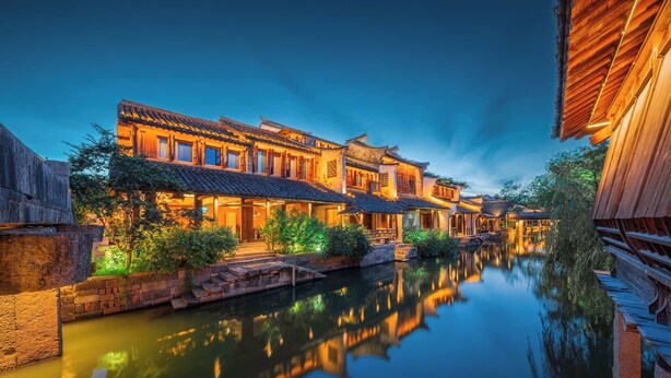 A traditional courtyard with a calm waterway, wooden buildings, and a wooden bridge. - Pujin Hotel (Jiaxing)