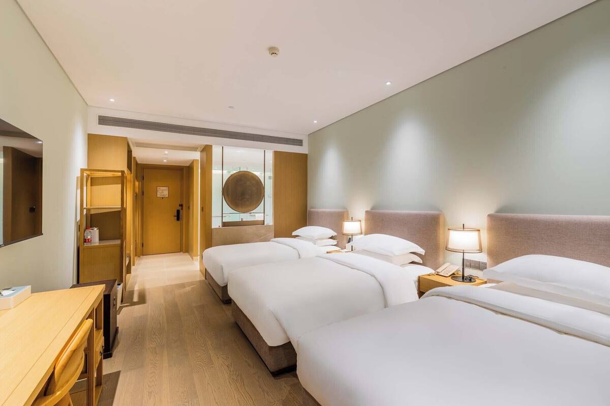 Habitación de hotel con tres camas, un escritorio y un espejo.