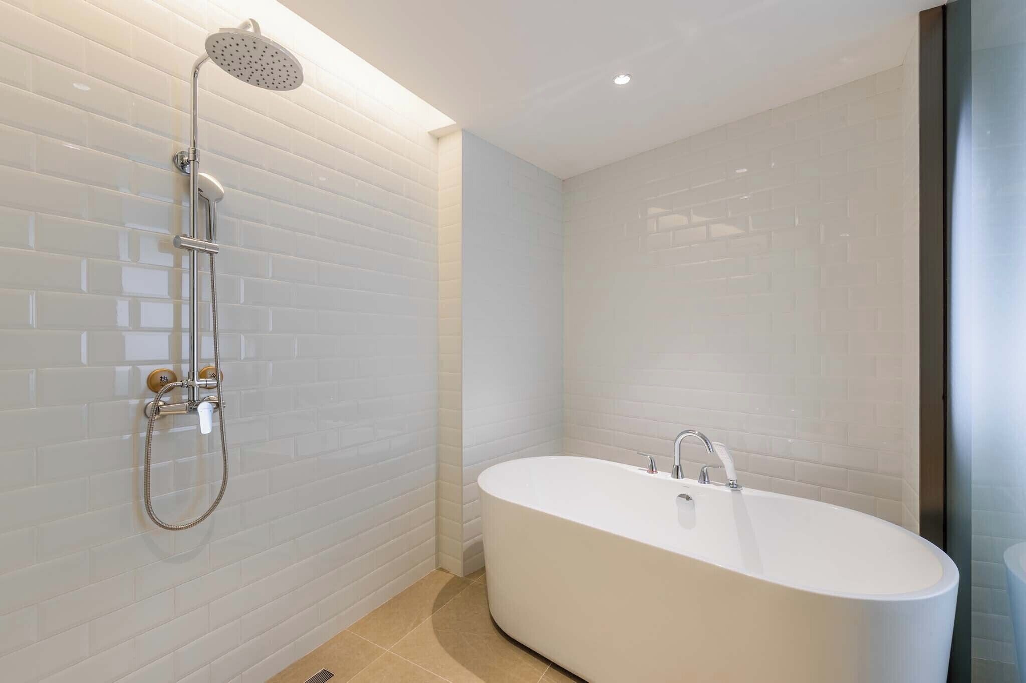 A modern bathroom with white subway tiles, a freestanding bathtub, and a walk-in shower with a handheld showerhead.