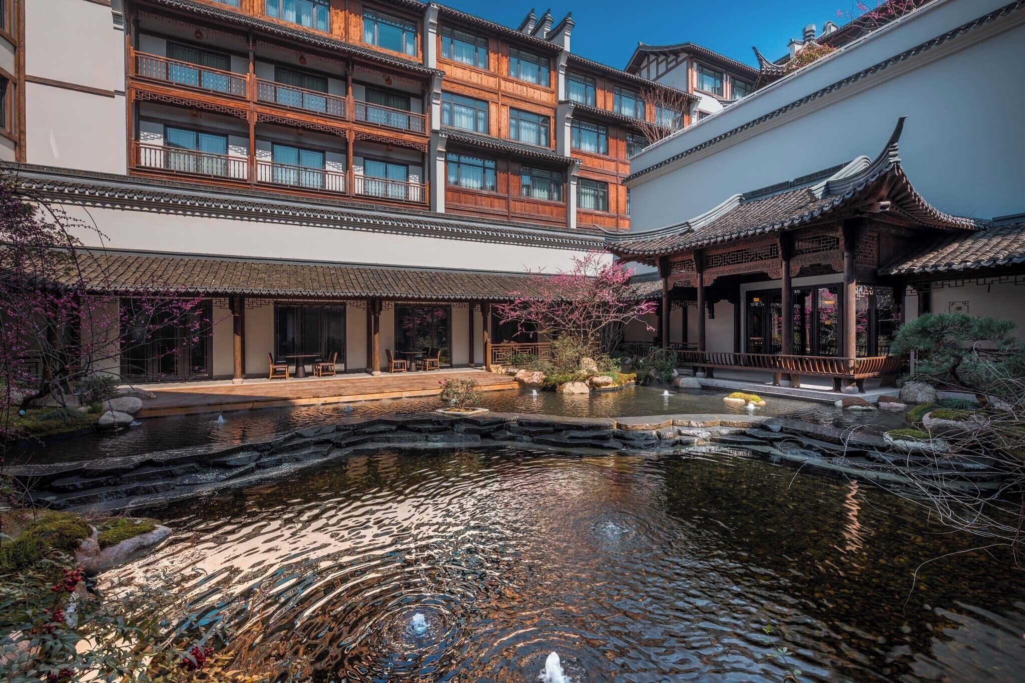 A traditional courtyard with a pond, wooden buildings with multiple balconies, and a covered walkway.