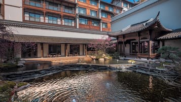 A traditional courtyard with a pond, wooden buildings with multiple balconies, and a covered walkway.