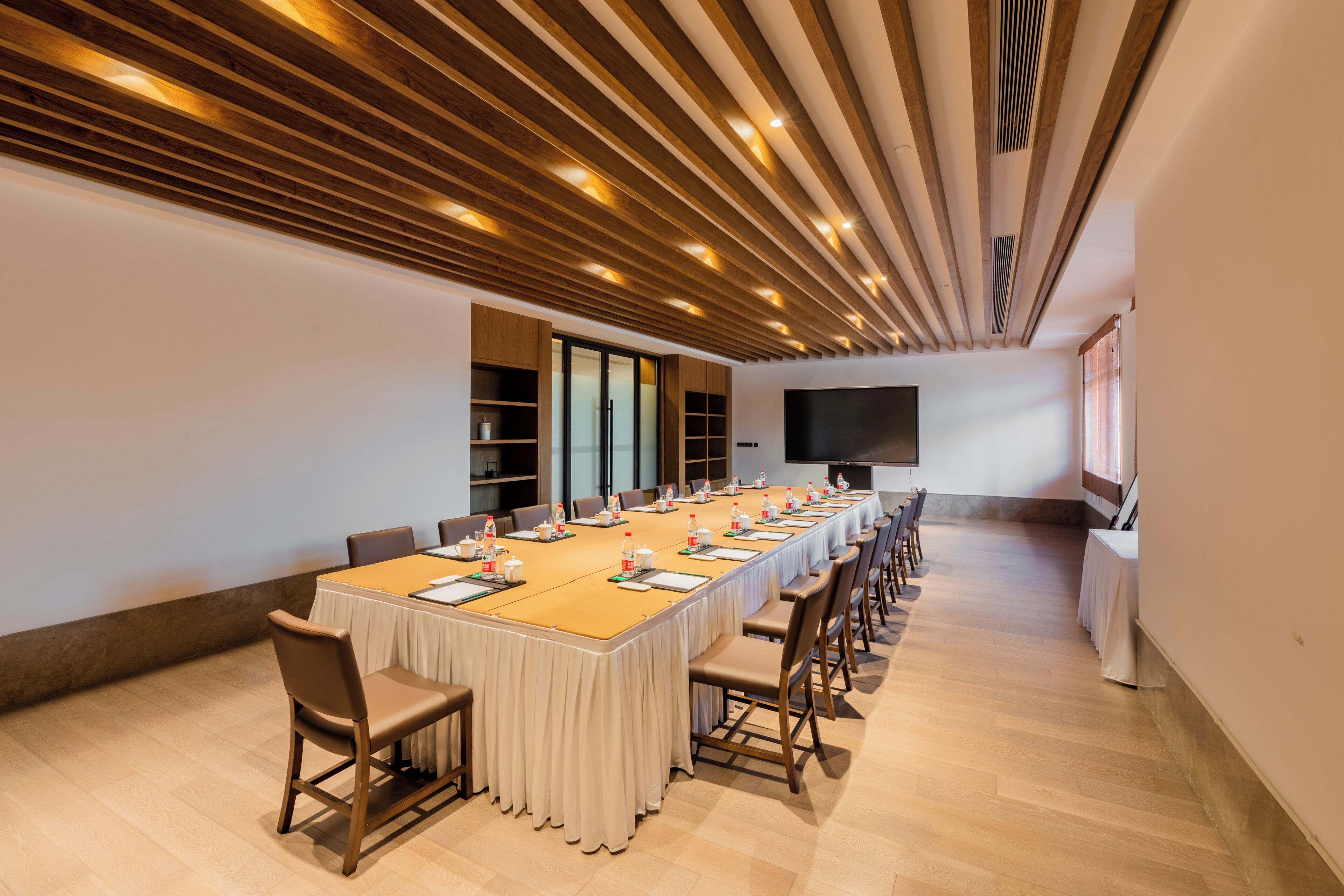 A conference room with a long table, chairs, and a large screen.