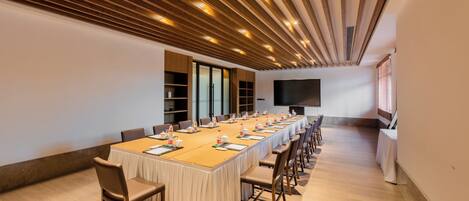 A conference room with a long table, chairs, and a large screen.