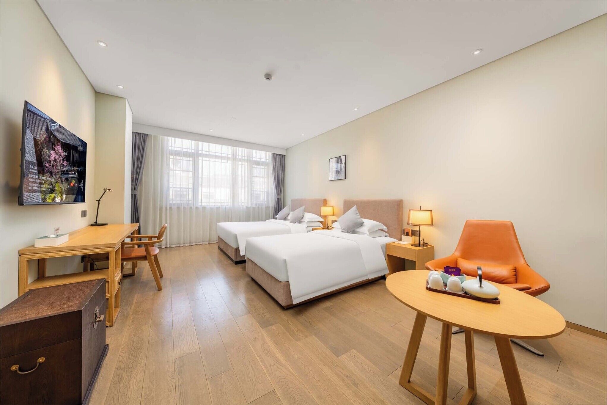 A hotel room with two beds, a desk, a chair, a small table, and a TV on the wall.