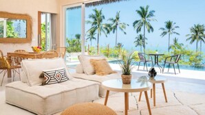 A modern living room with a large window overlooking palm trees and a pool. - 180° Sea View Villa | Private Infinity Pool Bang Por Koh Samui (Koh Samui)