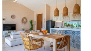A modern living room with a sofa, dining table, wicker chairs, a TV, and a kitchen area with hanging lights and a decorative backsplash. - 180° Sea View Villa | Private Infinity Pool Bang Por Koh Samui (Koh Samui)
