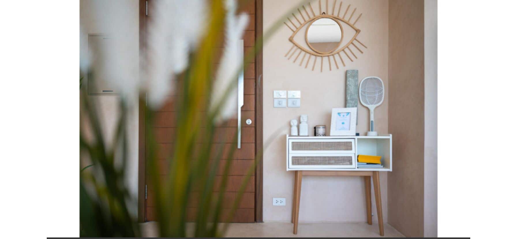 Una stanza con una porta in legno, un tavolino consolle bianco con uno specchio, una sveglia a parete e un quadro incorniciato.