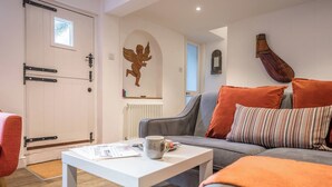 Ein modernes Wohnzimmer mit einem grauen Sofa, orangefarbenen Kissen, einem weißen Couchtisch und einem Wandbild eines Engels.