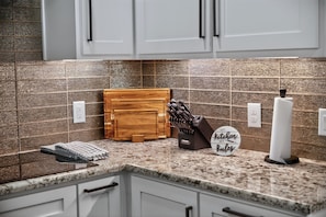 Una cocina con encimera de granito, tabla de cortar de madera, bloque de cuchillos y un letrero que dice 'My Kitchen My Rules'.